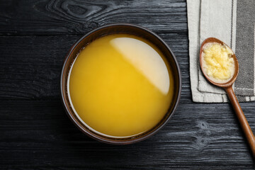 Bowl and spoon of Ghee butter on dark wooden table, flat lay