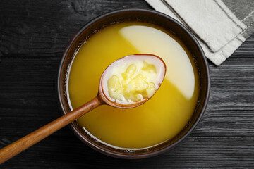 Bowl and spoon of Ghee butter on dark wooden table, flat lay