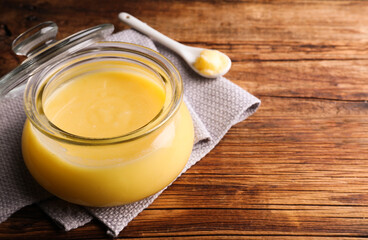 Glass jar and spoon of Ghee butter on wooden table, closeup. Space for text