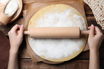 Woman rolling raw dough for traditional matzo at wooden table, top view