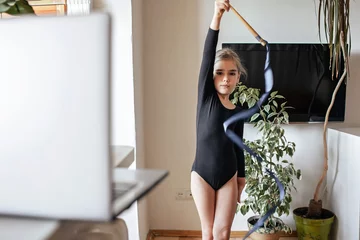 Tuinposter Pre teen girl in black sportswear watching world sport competition online and repeating exercises, rhythmic gymnastics, sport and health concept, social distant cheering © Maria
