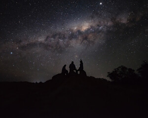 Naklejka na ściany i meble Silhouette of a group of person Sitting on a Rock Watching the Milkyway