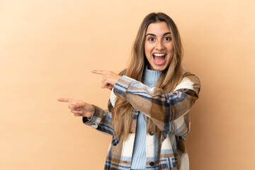 Young caucasian woman isolated on beige background surprised and pointing side