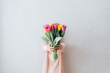 Portrait of woman with blonde hair hiding her face, and holding bouquet of pink and yellow tulip flowers. White background, copy space, close up.