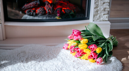 Fresh spring yellow and pink tulips bouquet on the fur carpet floor by the fireplace with copy space for text. Love, easter, International Women, Mother and Happy Valentine day concept