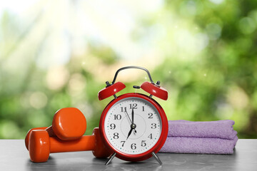 Alarm clock, towels and dumbbells on marble table outdoors. Morning exercise