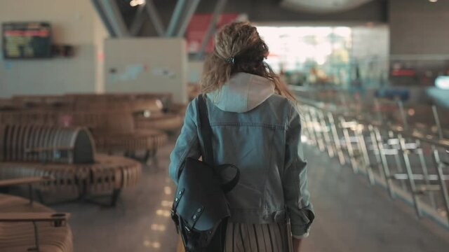Young female traveler with tiket and mask in airport walking hall, view of tourist with backpack crossing terminal for registration