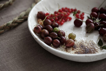 Craft white plate filled with gooseberries and red currants. Country rustic linen table set up