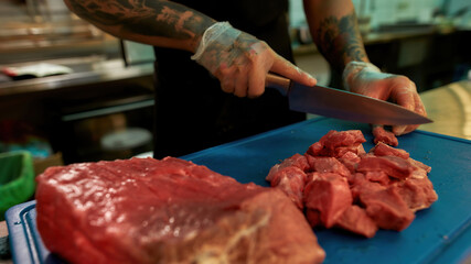 Close up of hands of male cook wearing protective gloves chopping raw pork meat on a plastic board...