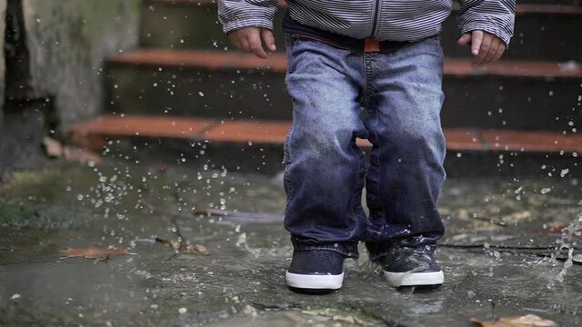 Child jumps into puddle in 240fps slow-motion. Kid having fun outside after rain