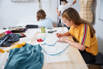 Cute girl drawing clothes patterns in sewing workshop