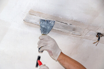 mans hand in cloth glove with spatula and putty, applies mastic to the wall, ceiling to level the...