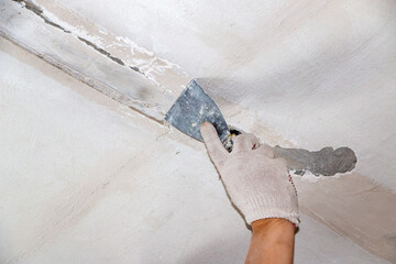 mans hand in cloth glove with spatula and putty, applies mastic to the wall, ceiling to level the...