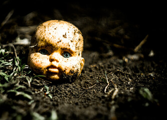 Old broken scary doll head on a ground in abandoned village.