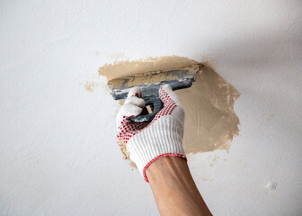 mans hand in cloth glove with spatula and putty, applies mastic to the wall, ceiling to level the...