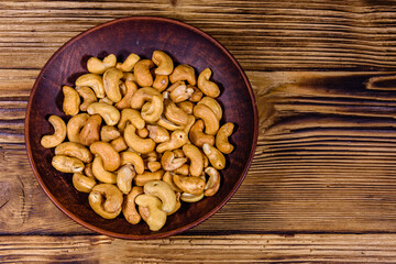 Ceramic plate with roasted cashew nuts on a wooden table. Top view