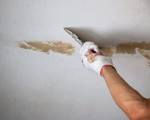mans hand in cloth glove with spatula and putty, applies mastic to the wall, ceiling to level the...