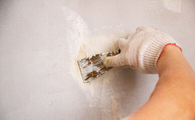 mans hand in cloth glove with spatula and putty, applies mastic to the wall, ceiling to level the surface. The process of applying mastic withspatula to the surface for interior design of the room.