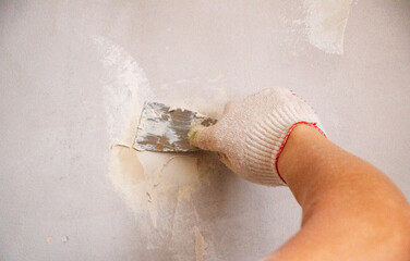 mans hand in cloth glove with spatula and putty, applies mastic to the wall, ceiling to level the...
