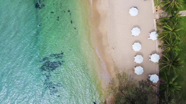 Aerial view of amazing turquoise sea and beach with white umbrellas and sun loungers. Beautiful sunny summer day in island Phu Quoc, Vietnam.