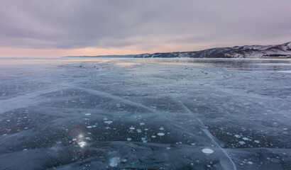 Winter sunset over Lake Baikal. The smooth surface of the ice is lined with cracks. White bubbles...
