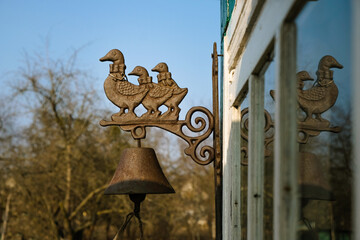 Home cast iron bell on the wall of an old wooden house in the golden hour on a background of the sky. Cast iron figurines of duck and ducklings.