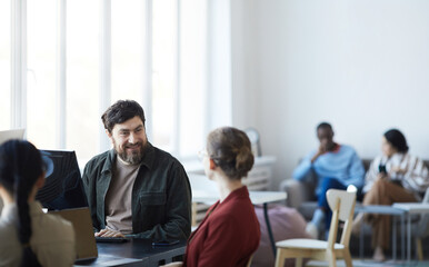 Portrait of smiling bearded man talking to female colleague during meeting in modern office, copy space