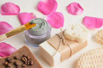 pink rose petals, cosmetic blue clay, washcloth, brush, loofah, cocoa soap and flowers on a light background spa concept