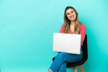 Young caucasian woman sitting on a chair with her pc isolated on blue background with arms crossed and looking forward