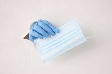 Hand in rubber glove pull out medical protective mask from torn paper