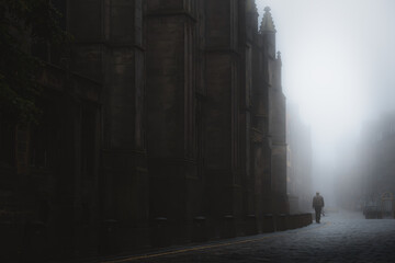 Silhouette of a man walking beside St Giles' Cathedral in moody atmospheric old town Edinburgh along the cobblestone Royal Mile in misty fog. - obrazy, fototapety, plakaty