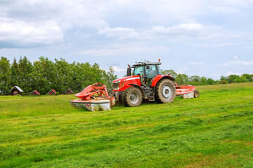 Big red tractor with two mowers mows the grass for silage