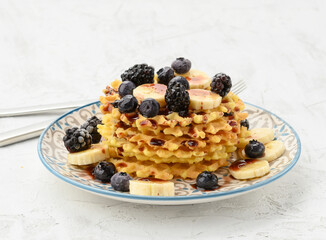 stack of baked Belgian waffles on a round plate with berries on a white table, delicious breakfast
