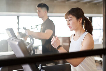 トレーニングジムでランニングマシンで走るアジア人女性