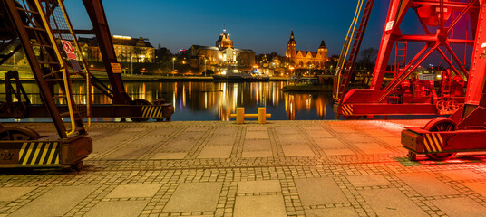 Illuminated old port cranes on a boulevard in Szczecin City at night.