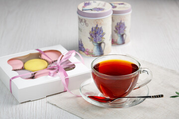 Multicolored macaroons in a box and a cup of tea on a light wood kitchen table. Morning tea and sweets.