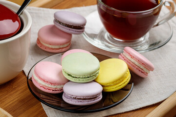 Multicolored macaroons and a cup of tea on a wooden tray. Morning tea and sweets.