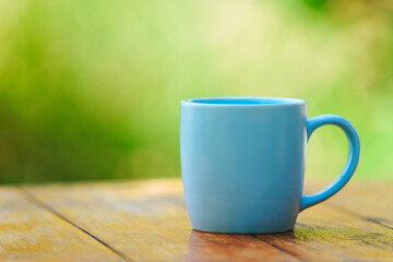 Simple blue ceramic mug on wooden table on green bokeh background. Copy space 