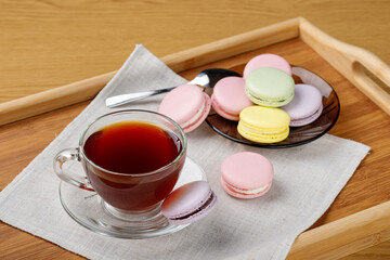 Cup of tea and colorful macaroons on a wooden tray. Morning tea and sweets
