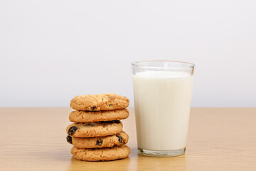 A glass of milk and cookies with raisins on the table.