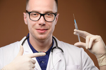 A young male Caucasian doctor holds a syringe with an injection in a gloved hand. Vaccines and...