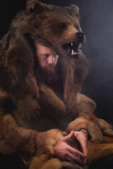 A male shaman werewolf in the skin of a bear sits in a dark room and reflects. Ancient warrior with...
