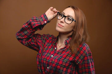 Naklejka premium Attractive young Caucasian female student holding glasses looks to the side. Studio portrait on brown background