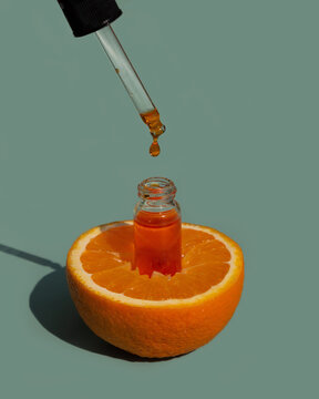 A Drop Of Orange Oil Or Serum Drips From A Pipette Into A Glass Cosmetic Bottle. Vitamin C Anti-aging Skin Care.