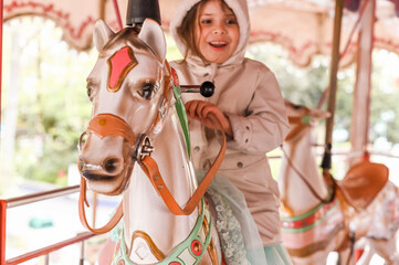 Little girl rides a carousel in an amusement park. Happy child