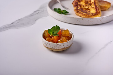 Melon jam with mint in a small bowl on a light background. In the back is Torrihas. Copy space