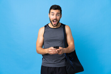 Young sport man with sport bag isolated on blue background surprised and sending a message