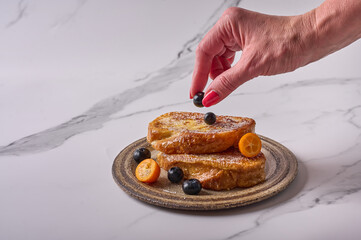 Woman's hand puts a blueberry on homemade traditional Spanish torrijas or French toasts. Popular dessert for Christmas, Easter or Pascua. Top view