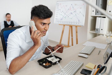 Stock market broker eating lunch at his office desk and answering phone call from client