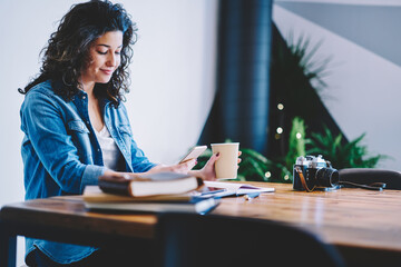 Charming female student with caffeine beverage using smartphone application for booking online education courses, Caucaisan hipster girl reading content publication browsing social media on mobile